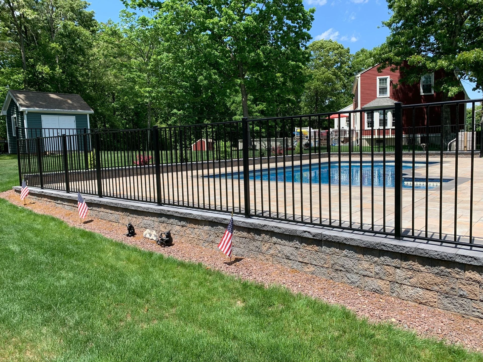 A good-looking black fence surrounds a swimming pool in a backyard.