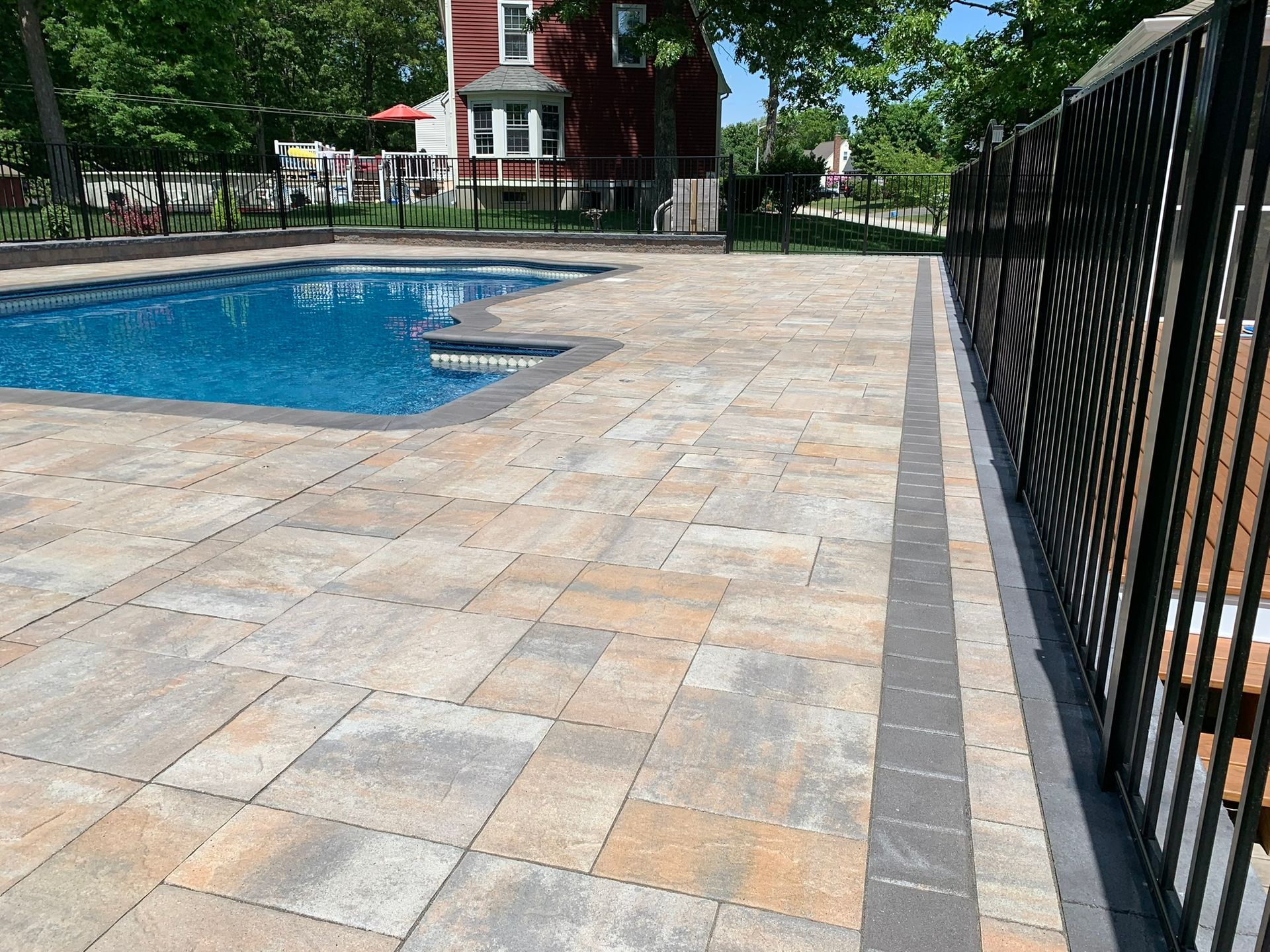 A large swimming pool is surrounded by a fence and a patio.