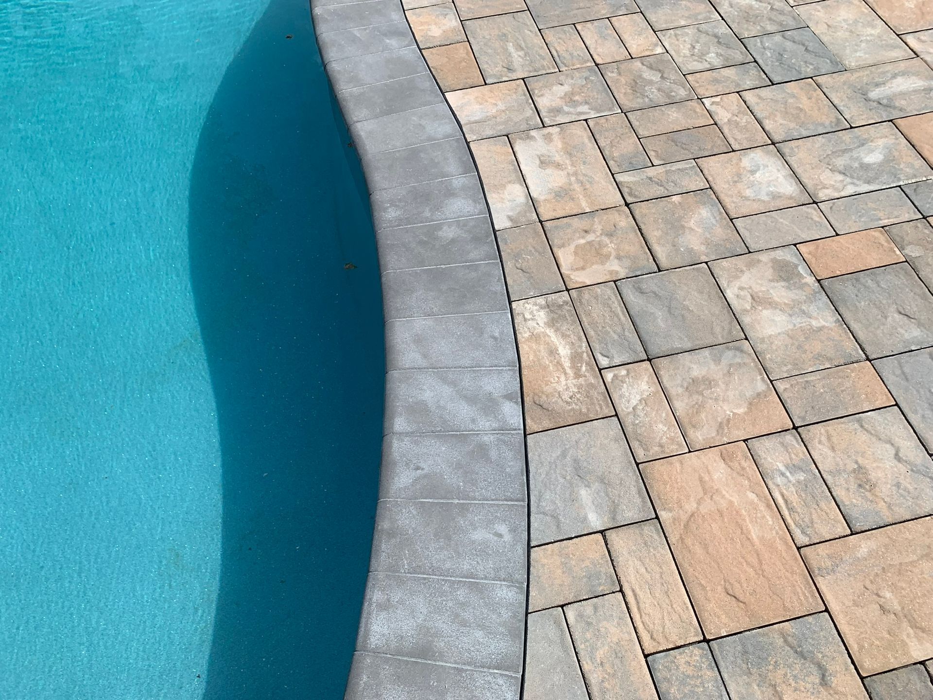 A brick walkway next to a swimming pool with a blue water.