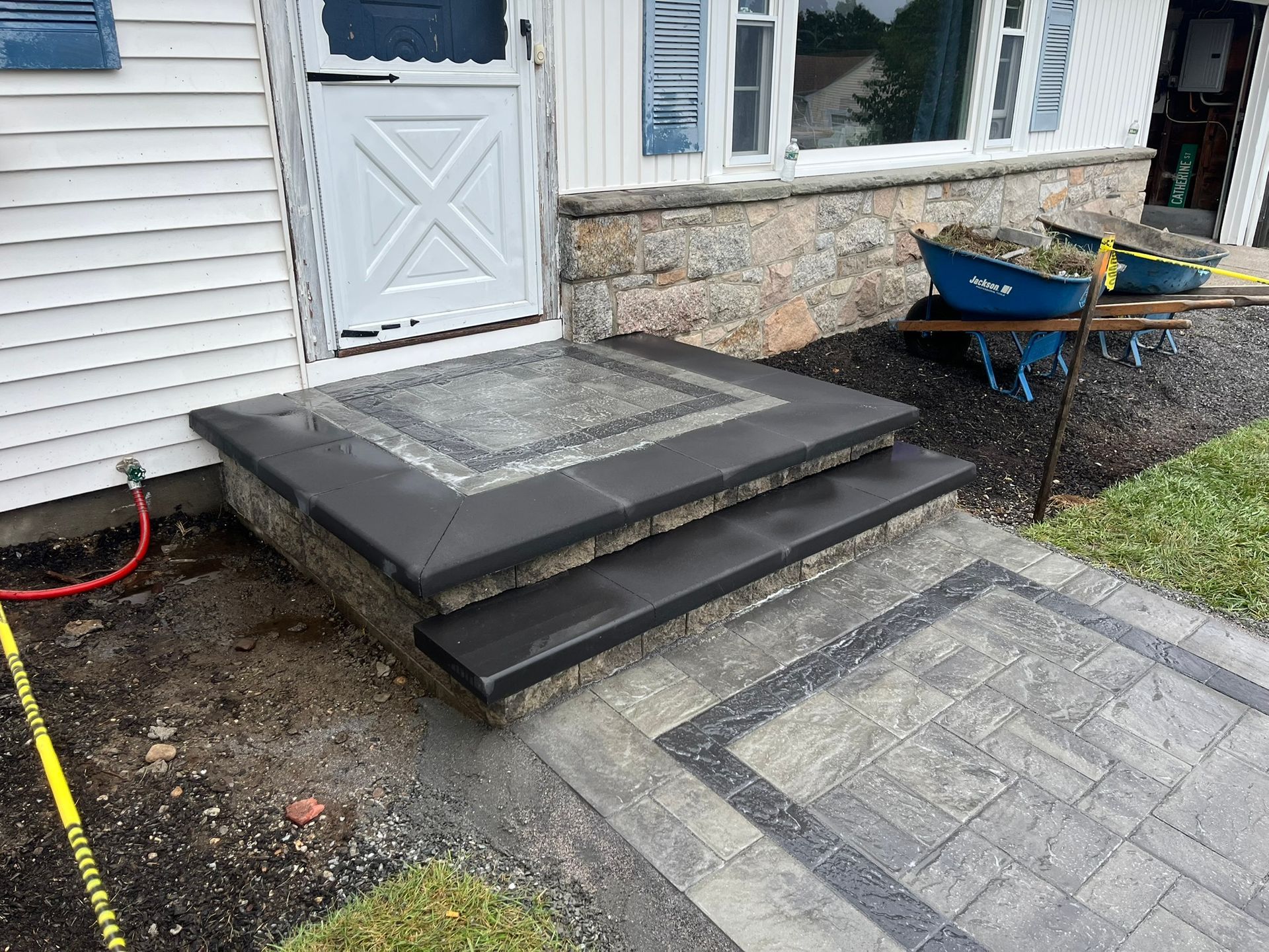 A house with stairs and a wheelbarrow in front of it.