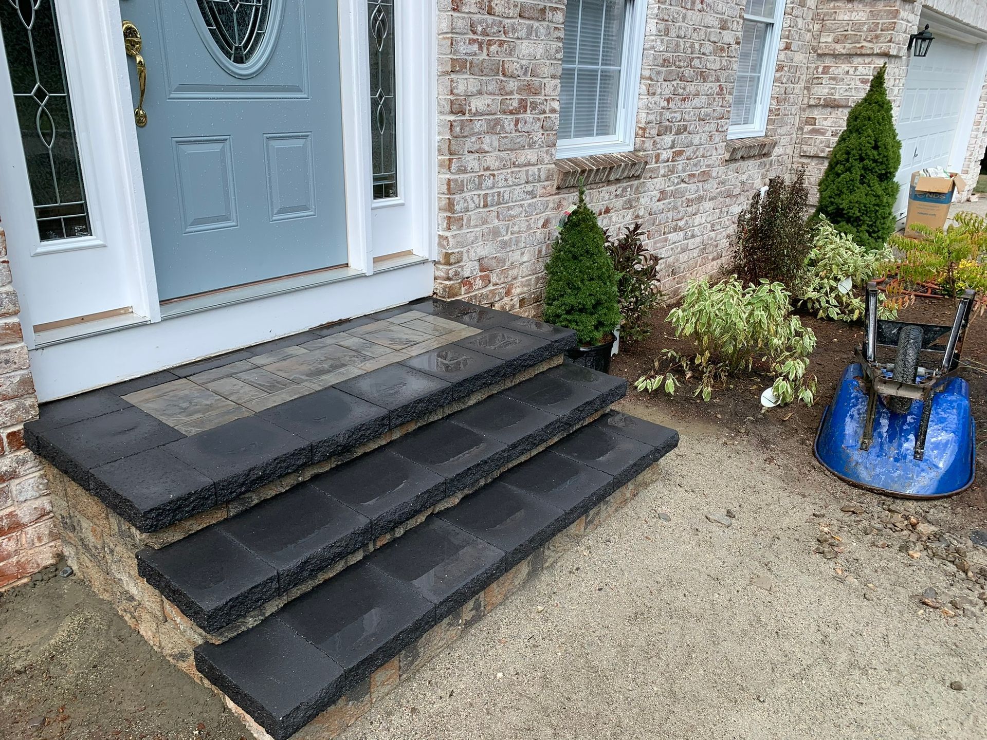 A blue snow blower is parked in front of a brick house.