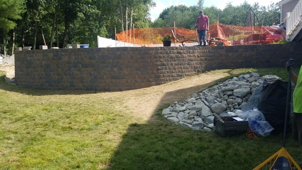 A man is standing next to a brick wall in a yard.