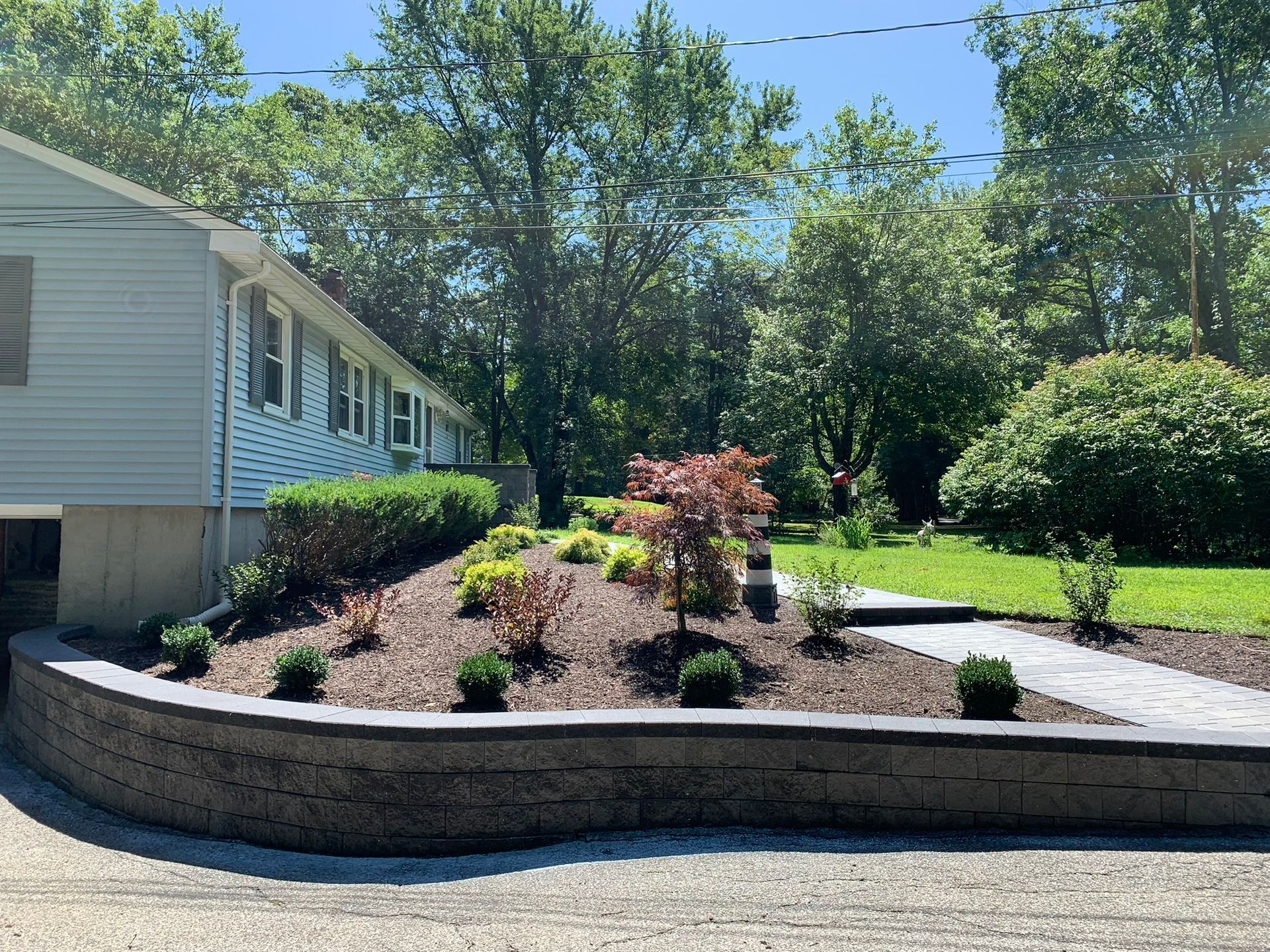 A house with a lush green yard and a stone wall in front of it.