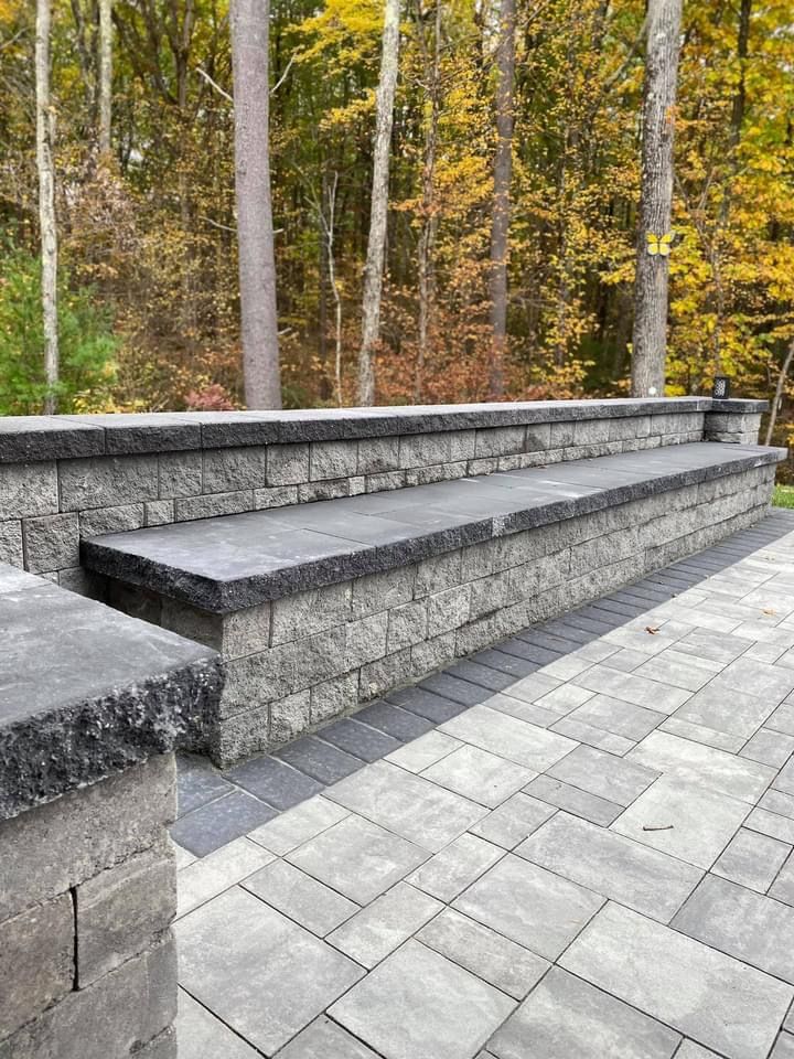 A brick wall with a bench on top of it and a patio with trees in the background.