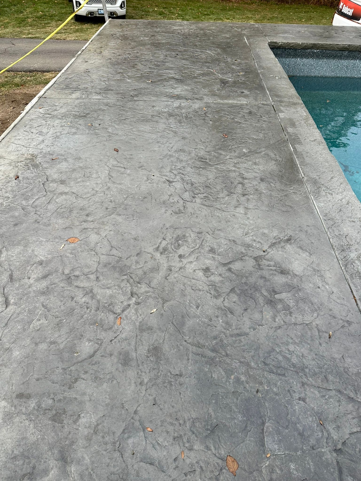 a concrete patio next to a swimming pool with a car parked on the side of it .