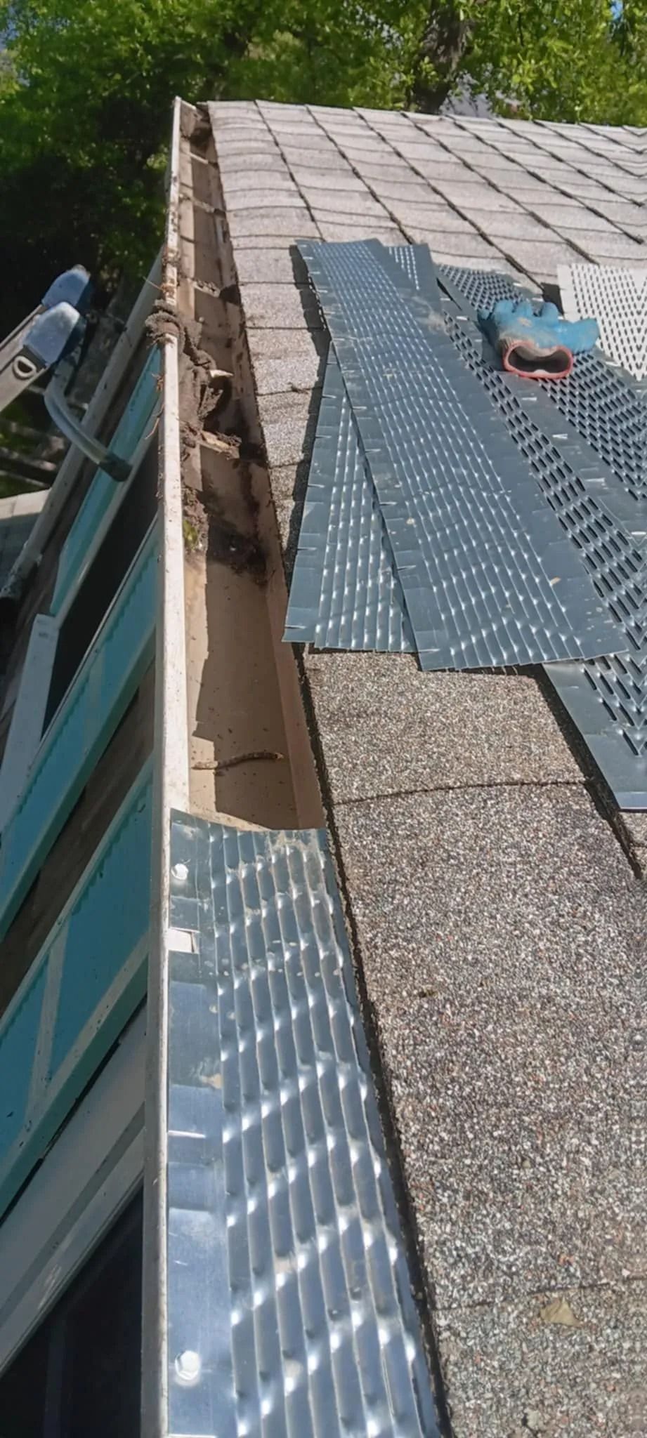 Roof with mixed shingles and metal flashing, showing a damaged or patched section along the edge