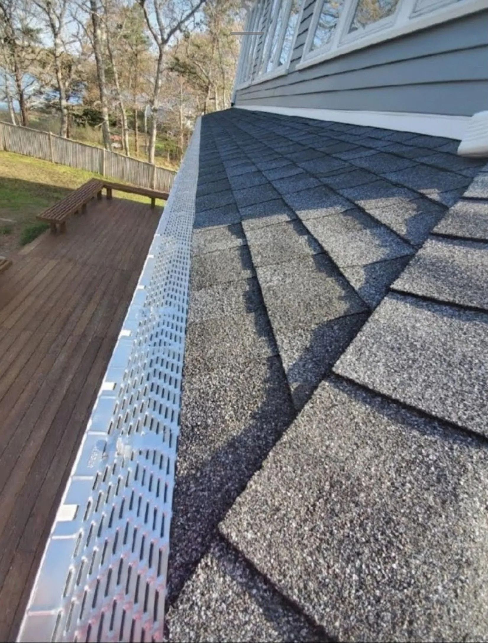Close-up of gray shingle roof with white gutter guard along the edge beside a wooden deck