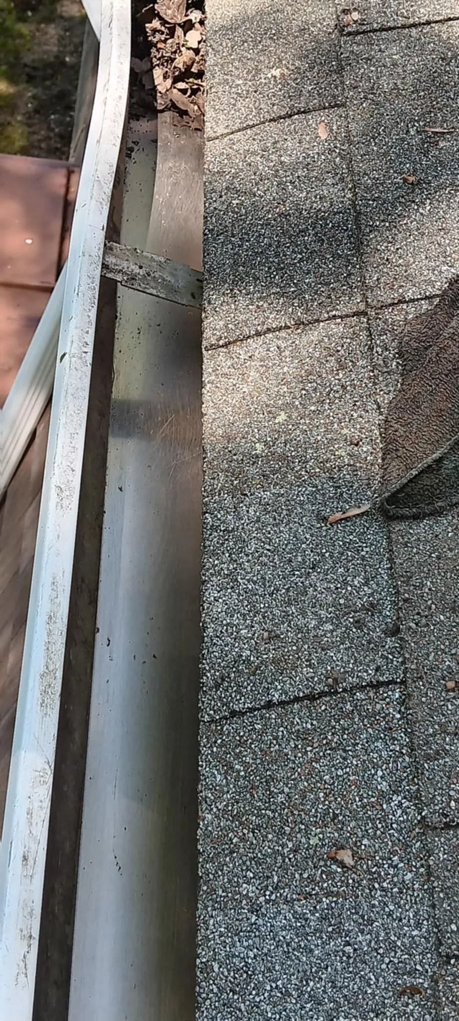 Close-up of a gravel roof edge with a white gutter and red shingles visible on the left