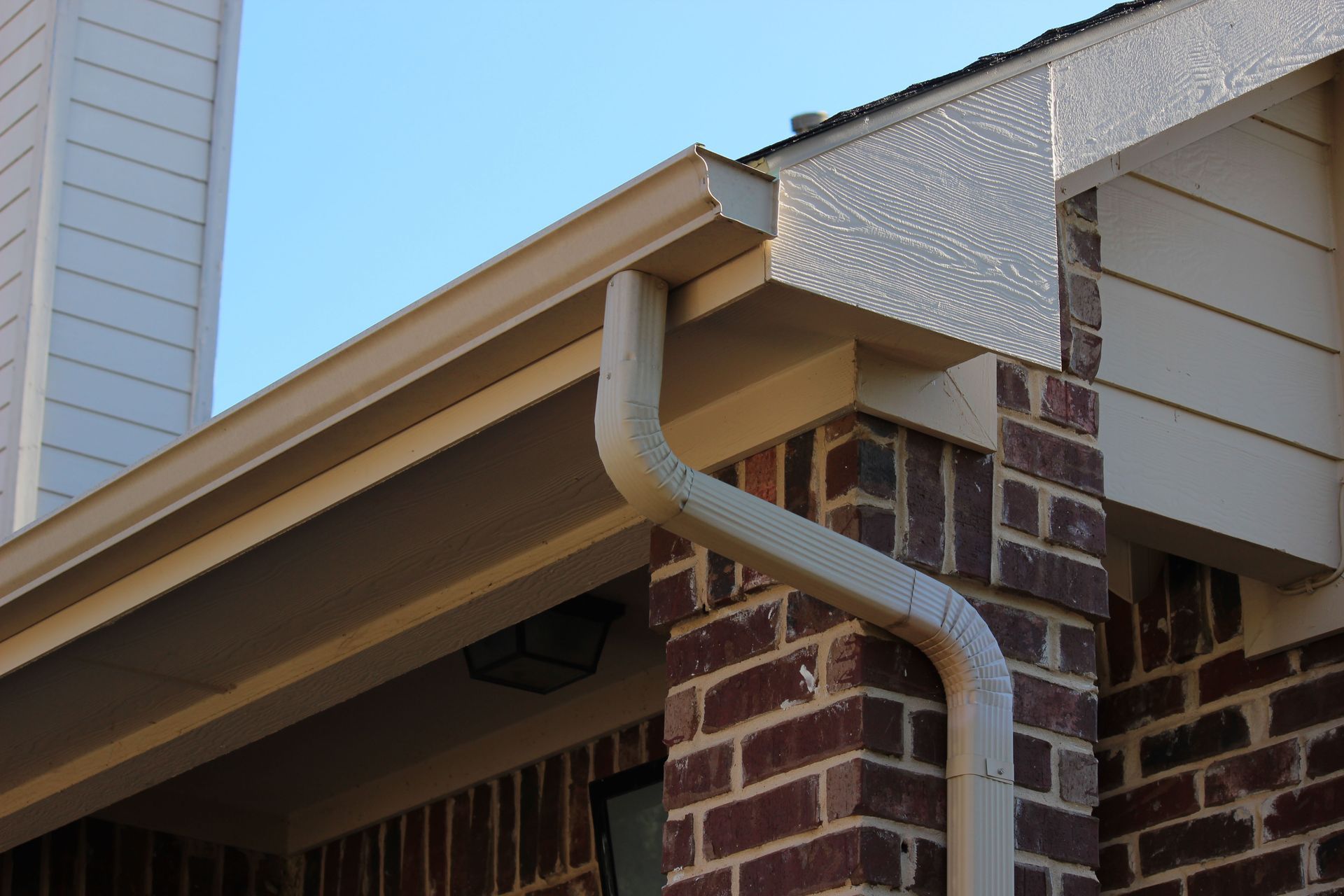 Gutter and downspout on a brick house roof corner with beige trim