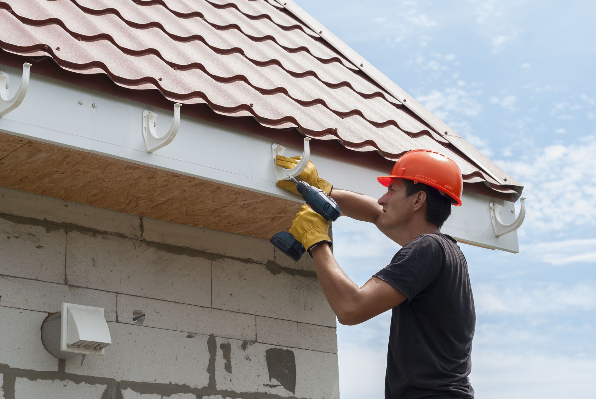 Worker using a power drill to install guttering on a house roofline