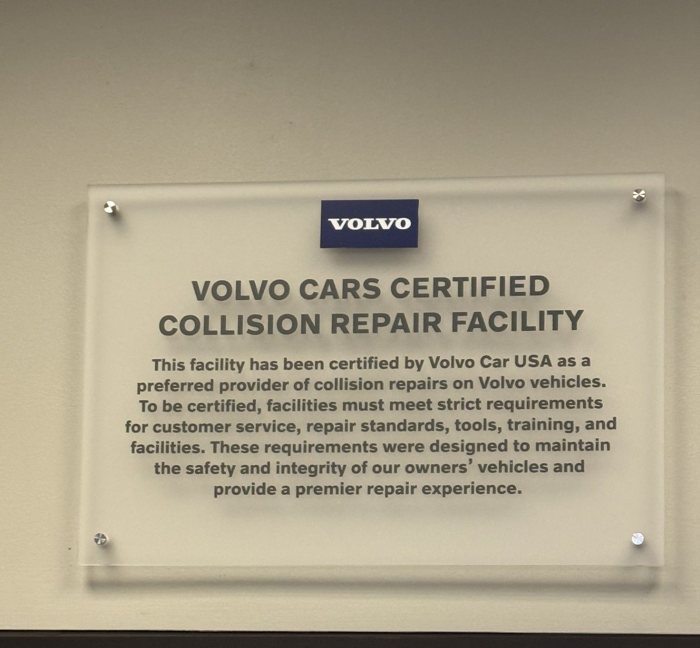Sign for a Volvo Cars certified collision repair facility. The sign is mounted on a wall and has the Volvo logo.
