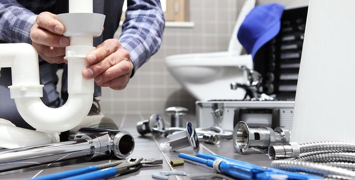 A plumber is fixing a pipe in a bathroom.