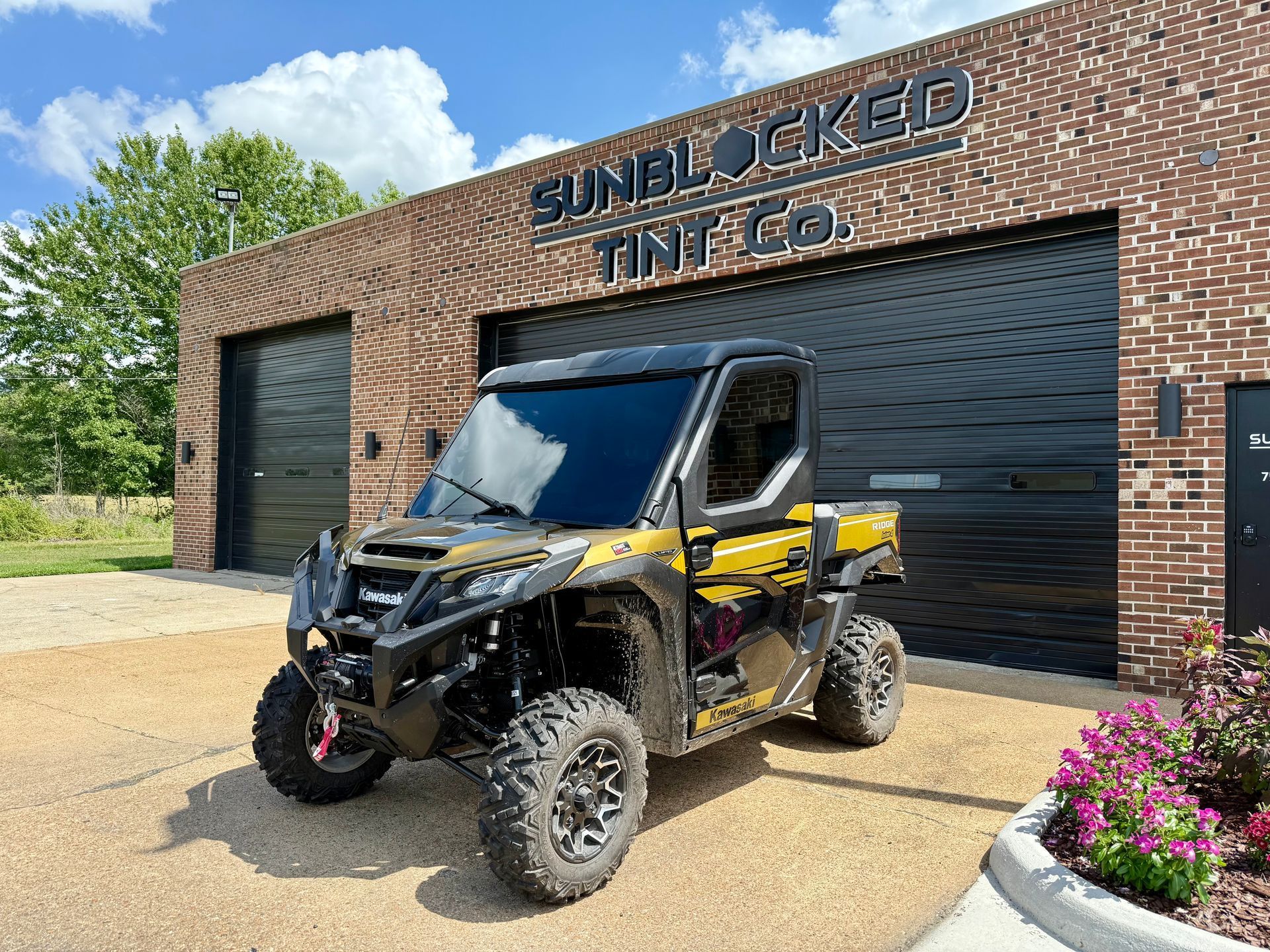 A yellow and black side-by-side vehicle parked in front of a brick building labeled 