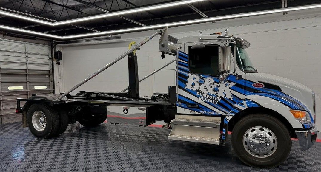 Roll-off truck with blue and white graphics, in a garage.