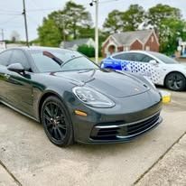 Dark gray Porsche parked outdoors near a white car with blue and white designs.