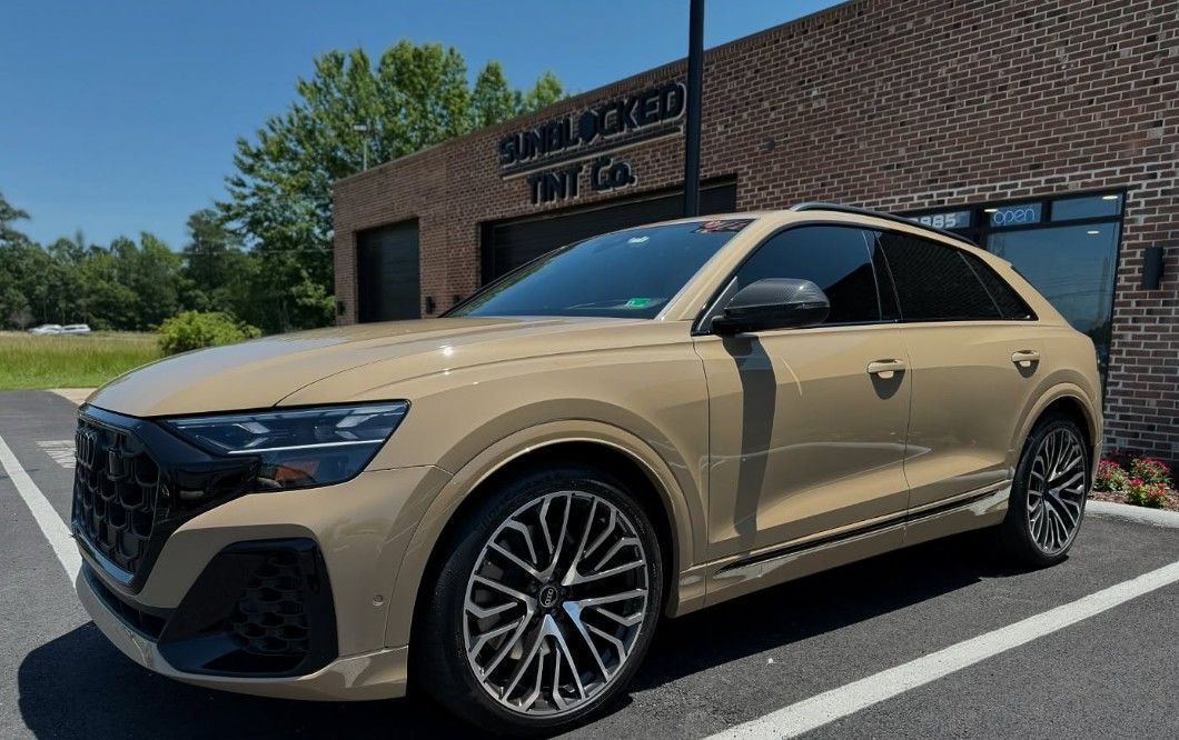 Tan Audi SUV parked in front of a brick building with tinted windows.