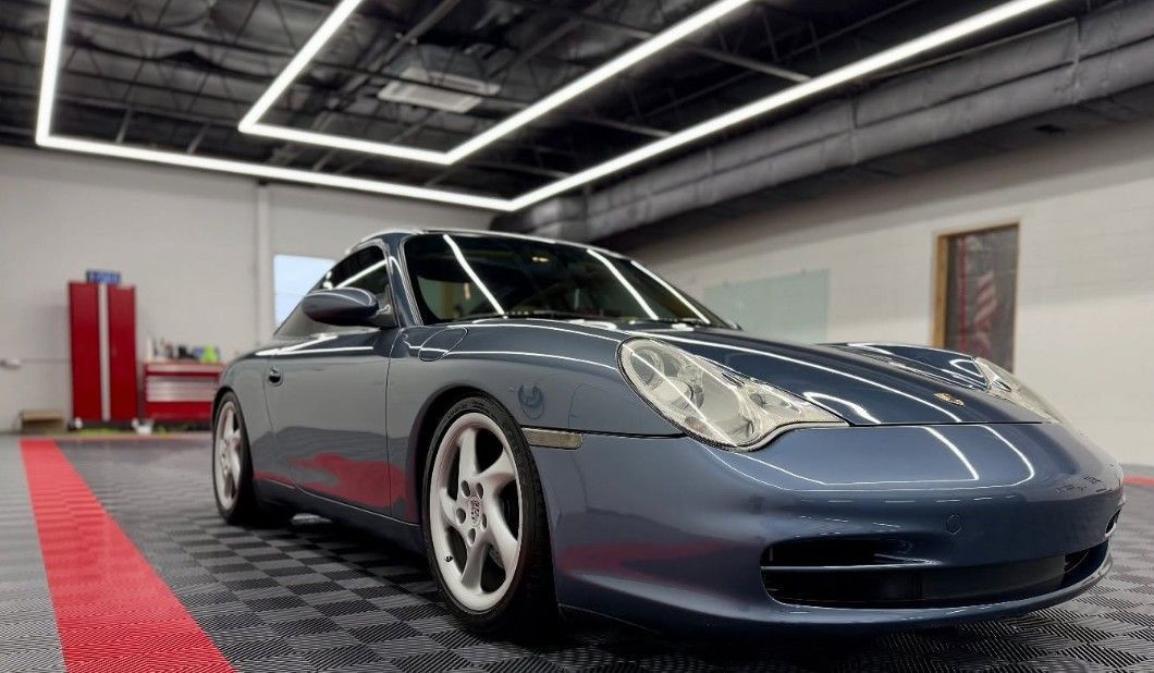 Blue Porsche 911 coupe parked in a well-lit garage with red and black flooring.