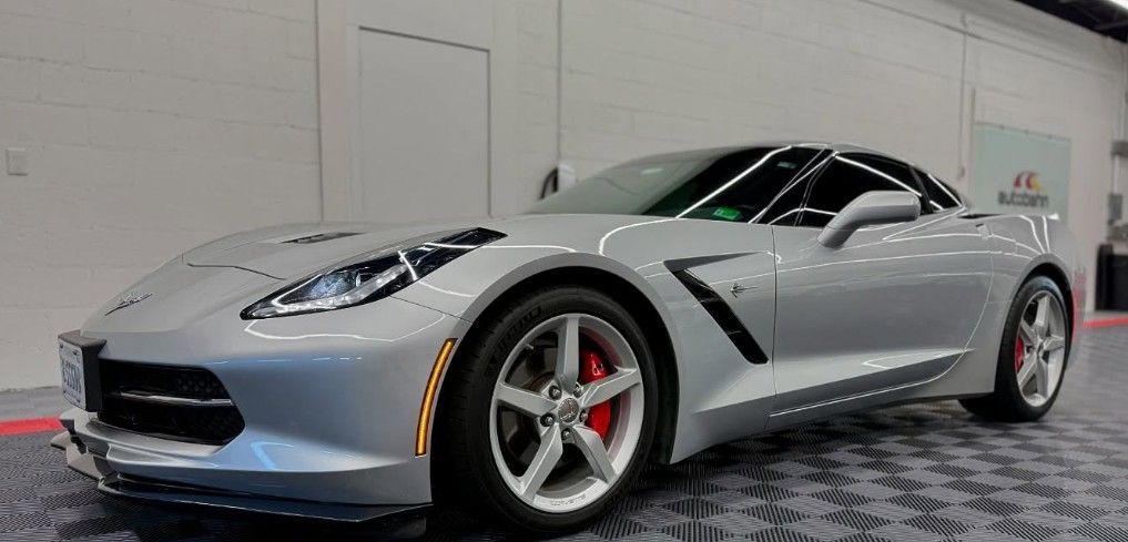 Silver Chevrolet Corvette sports car in a showroom with a black roof and red brake calipers.