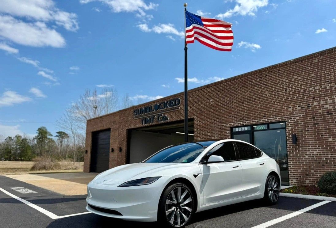 A white Tesla was parked in front of a brick building with an American flag.