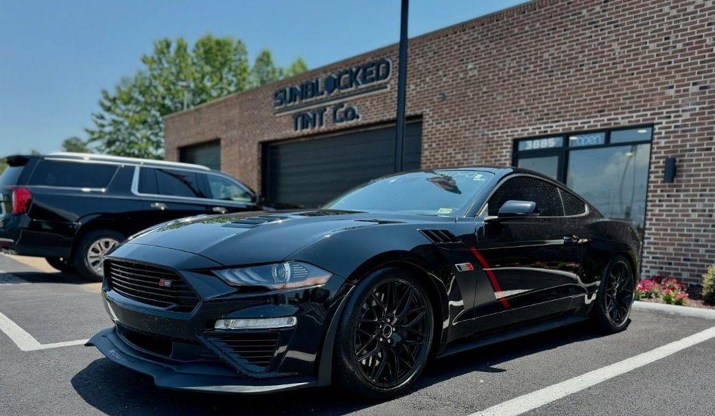 A black Ford Mustang is parked in front of a brick building.