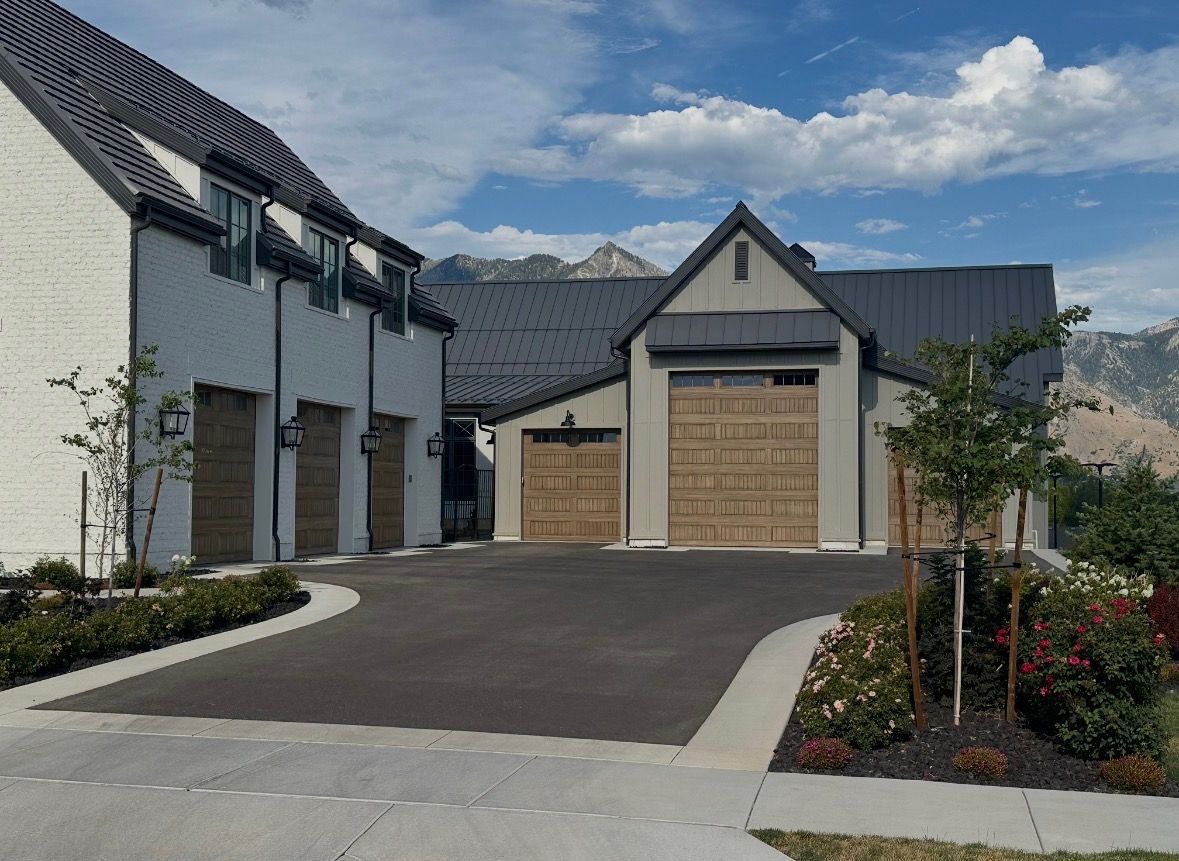 Modern suburban home exterior with a dark driveway, garage doors, and landscaped front yard under a blue sky