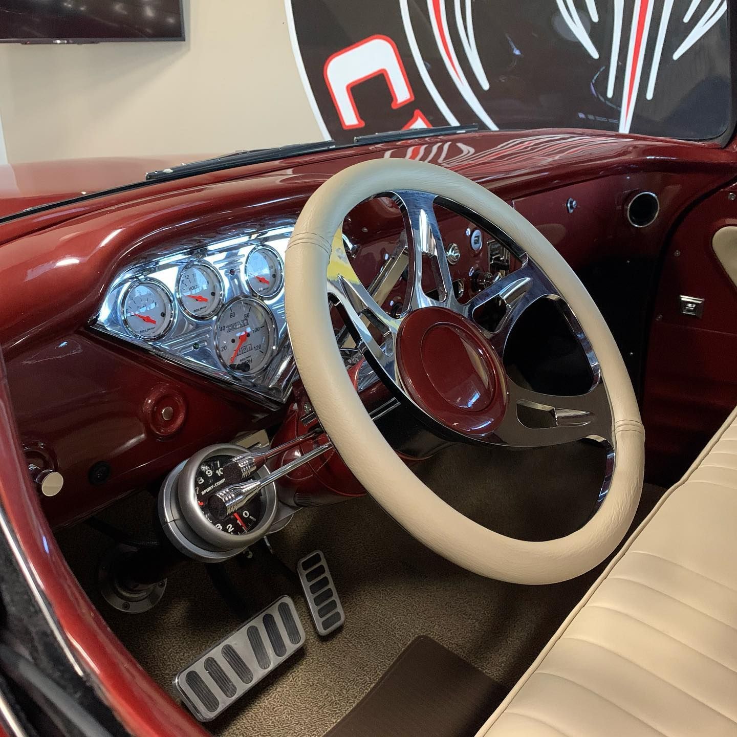 Red car interior with chrome steering wheel, gauges, and pedals; tan steering wheel cover and seat.