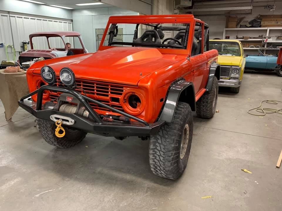 Orange off-road Bronco in a garage, modified with a winch, roll cage, and large tires.