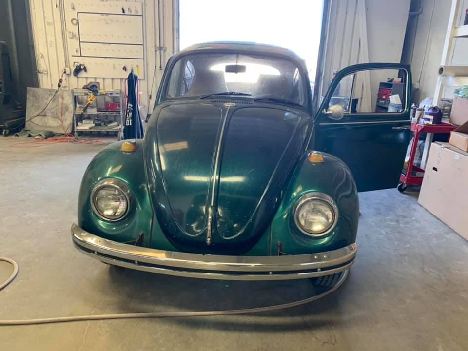 Green vintage Volkswagen Beetle car with the driver-side door open, in a garage.