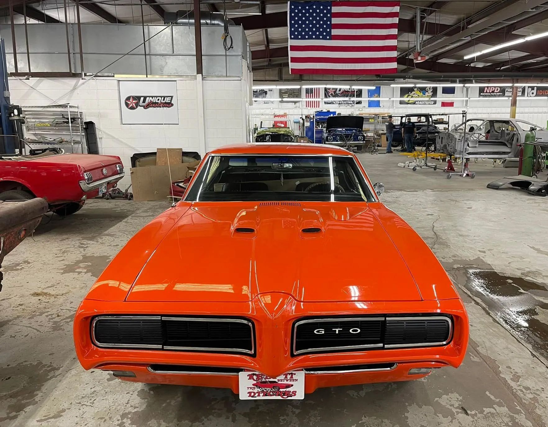 Bright orange Pontiac GTO muscle car in a garage with an American flag.