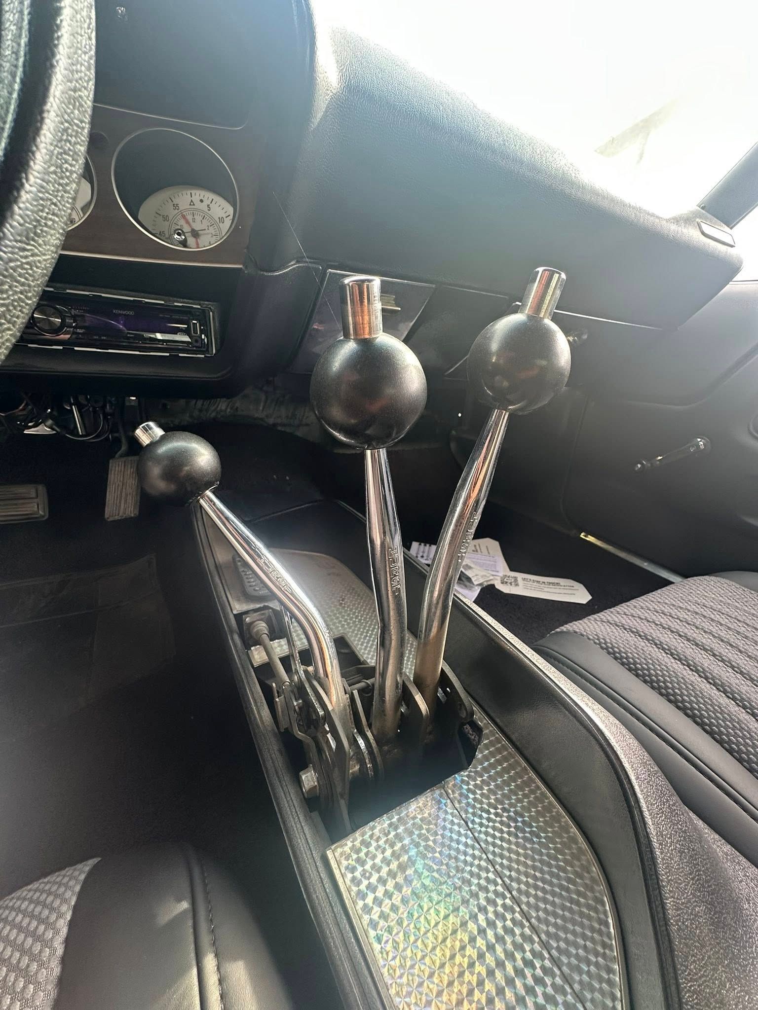 Classic car interior with three gear shifters, black and chrome accents, and a textured center console.