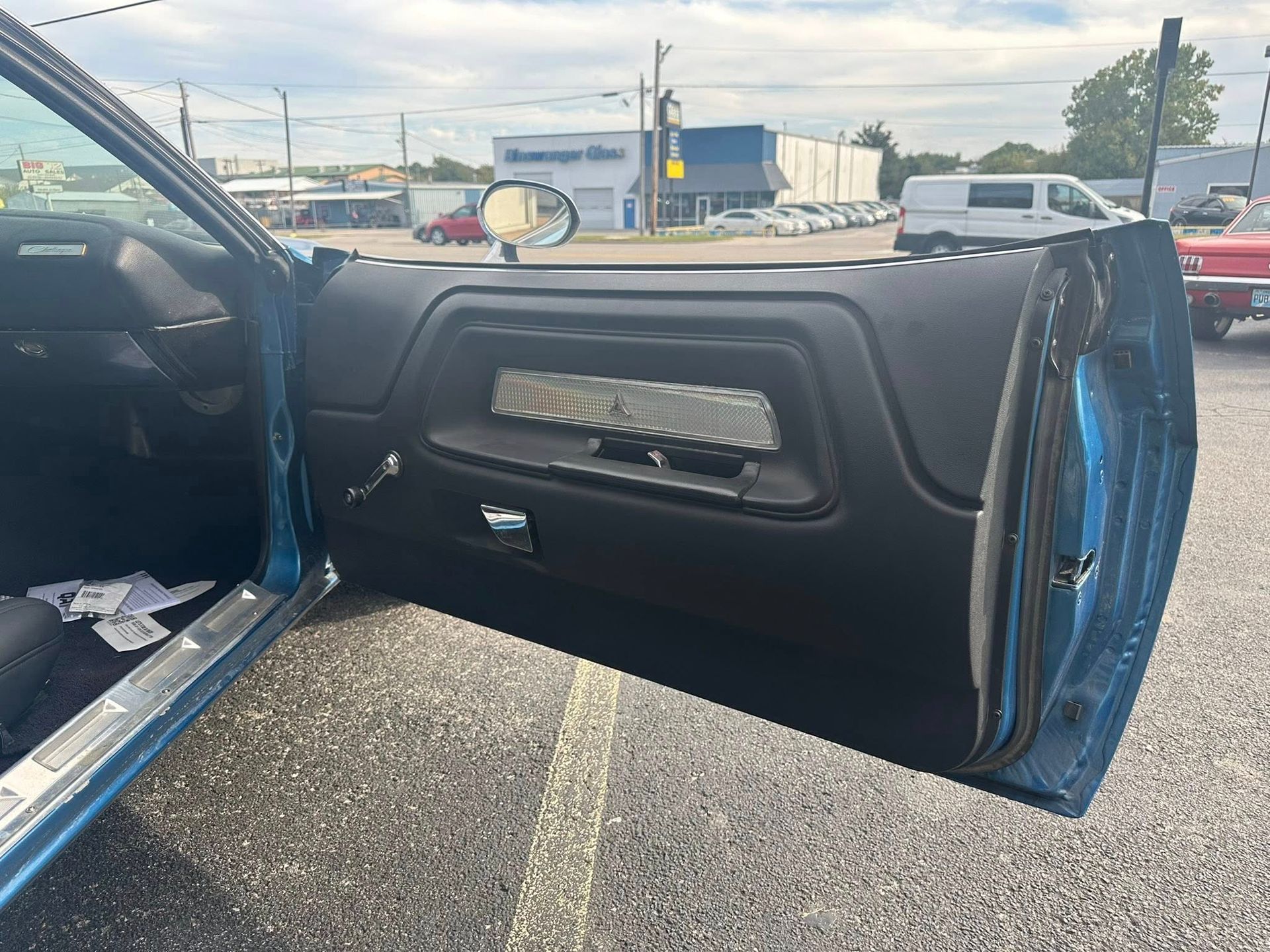 Open teal car door, black interior with window controls. Parked on asphalt.