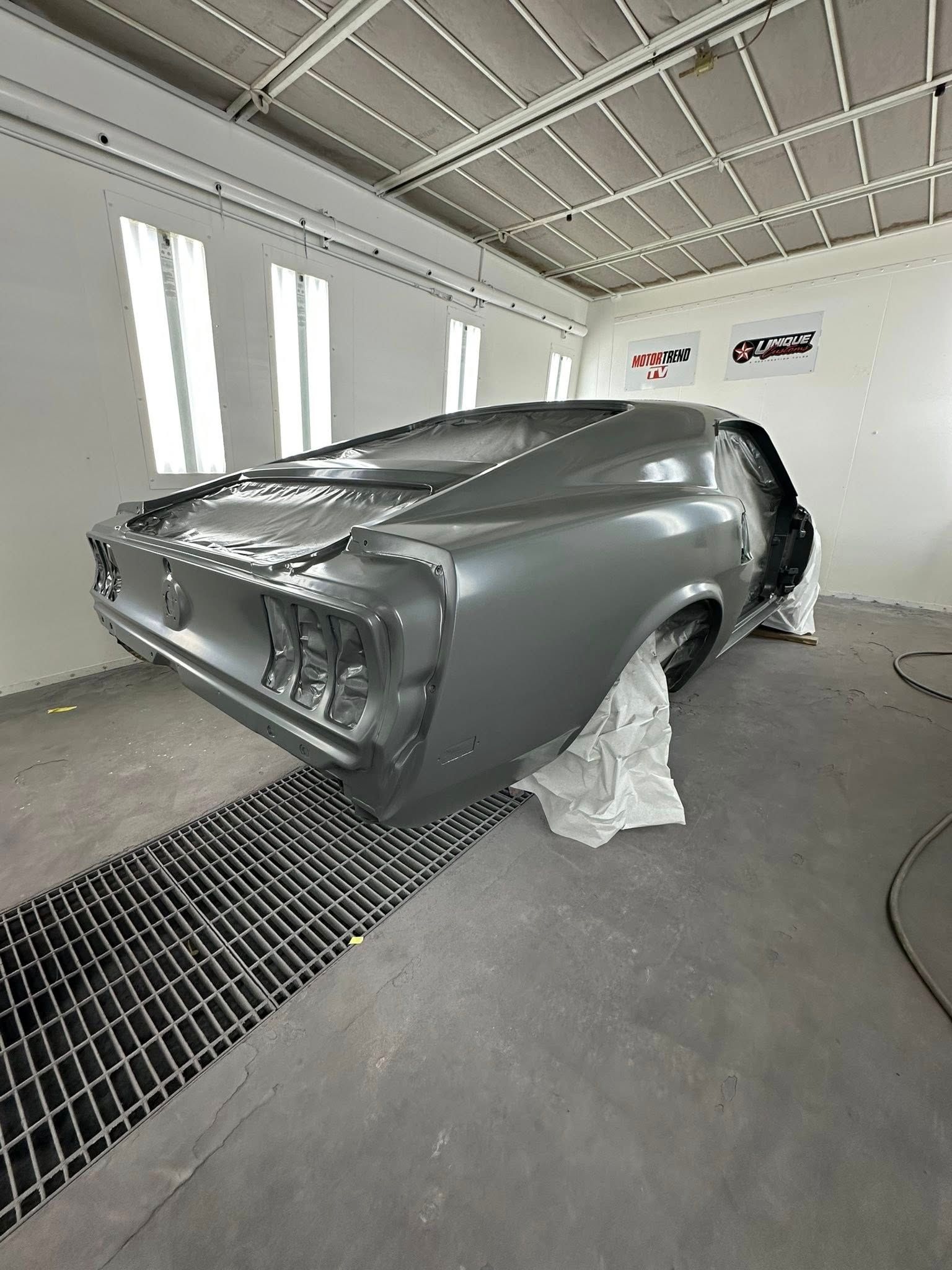 Classic gray muscle car in a body shop spray booth.