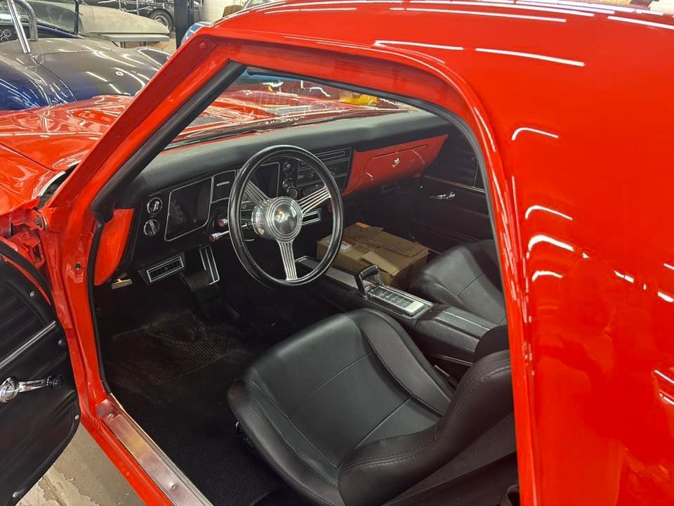 Interior view of a red classic car with black interior, including steering wheel, seats, and dashboard.
