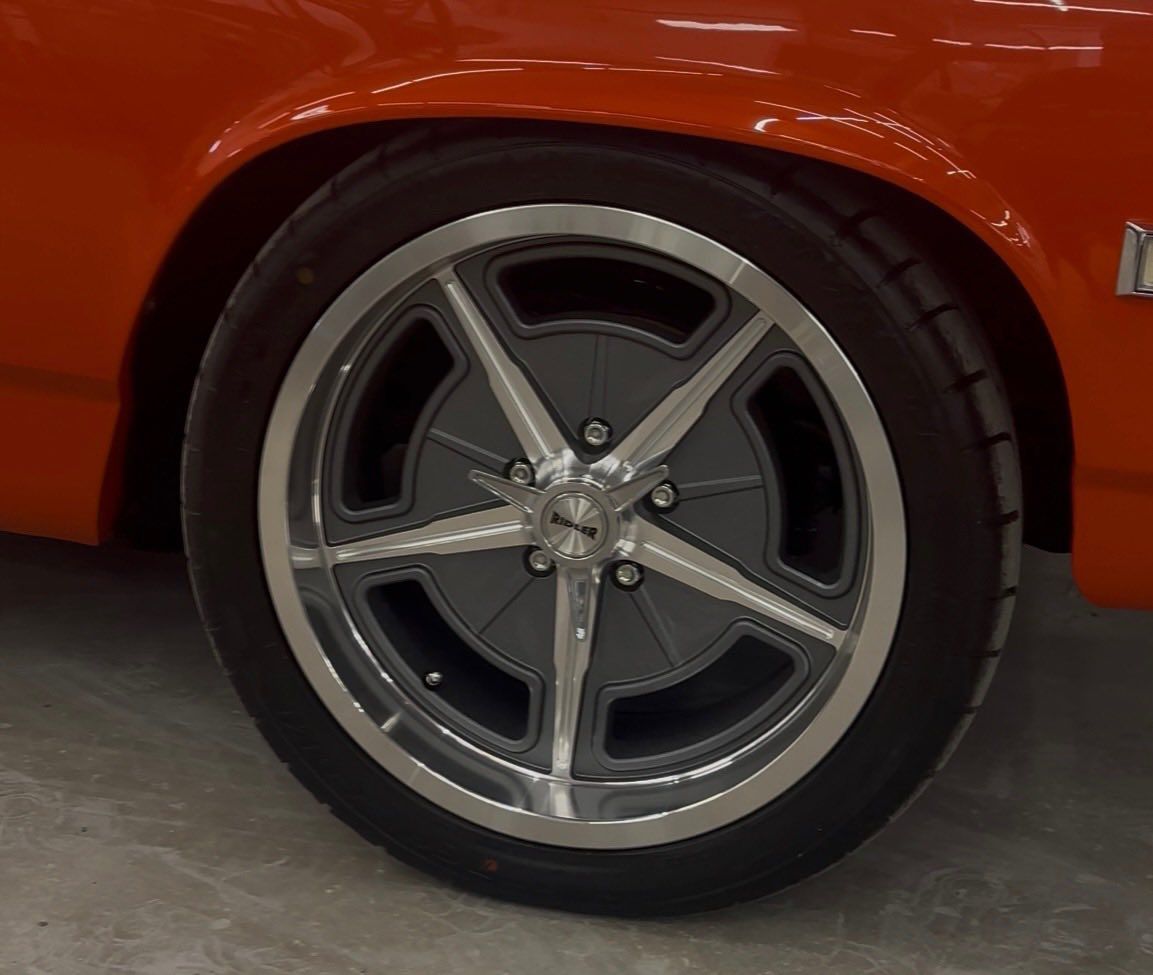 Close-up of a bright orange car wheel with a chrome and gray star-shaped rim and black tire.