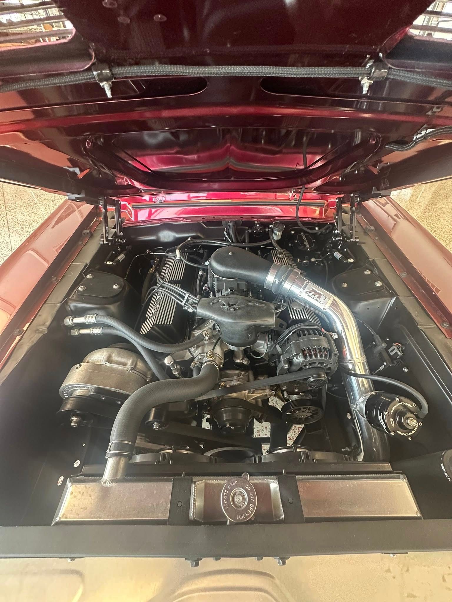 Open engine bay of a red classic car, displaying a black engine with chrome air intake.
