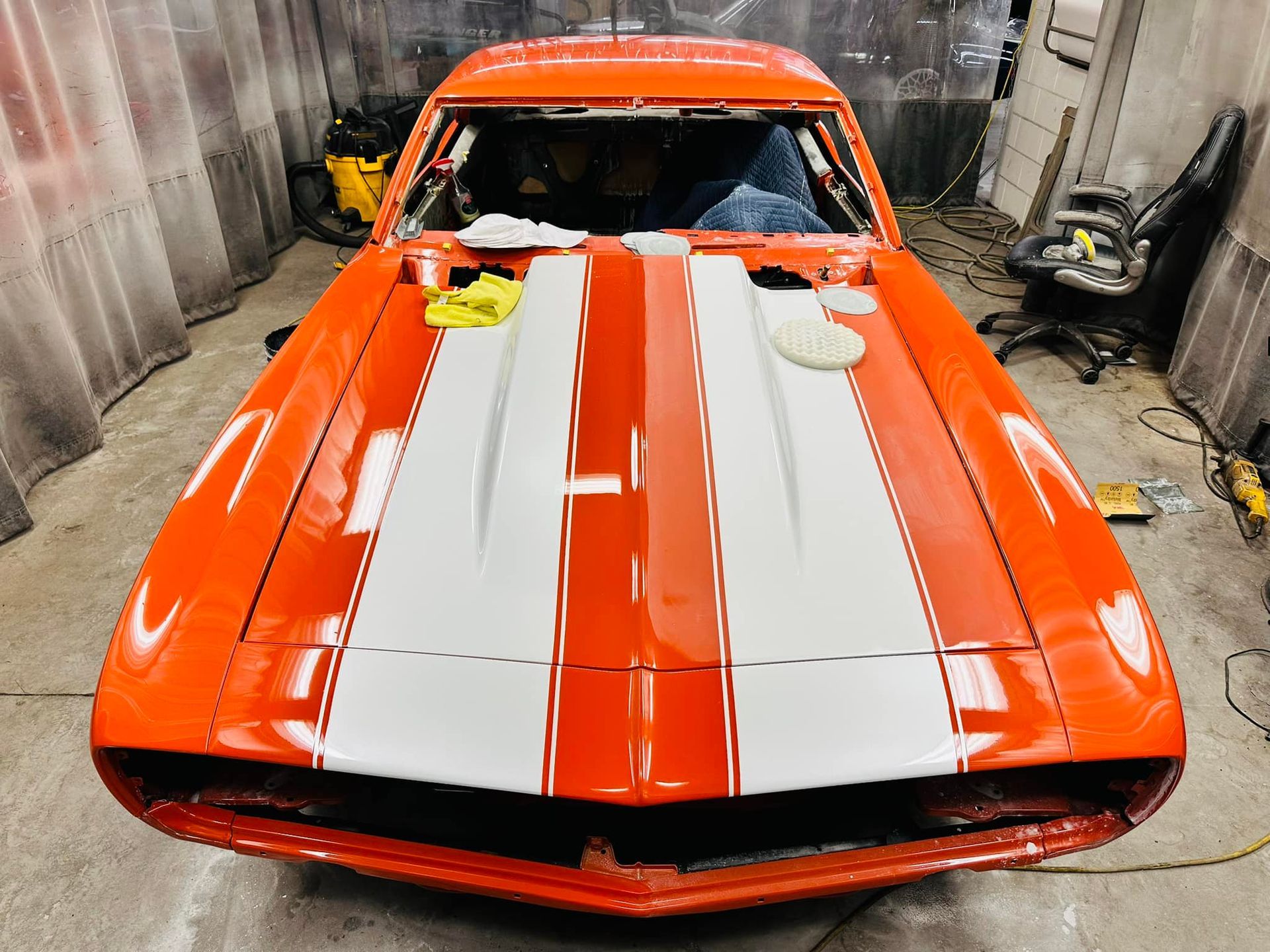 Bright orange classic car with white racing stripes in a garage.