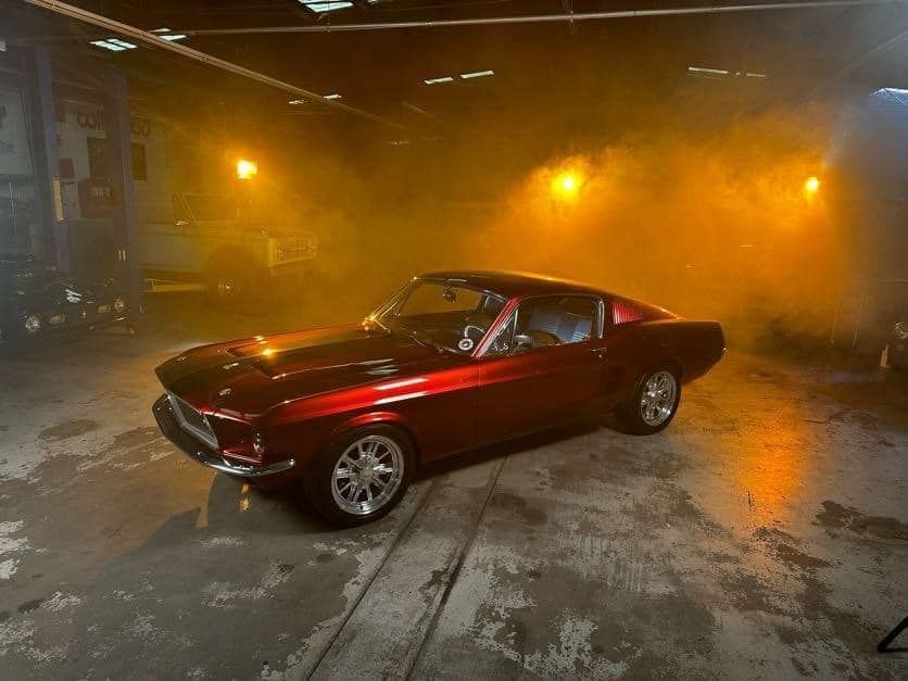 Red classic Mustang car in a smoky garage, illuminated by orange lights.