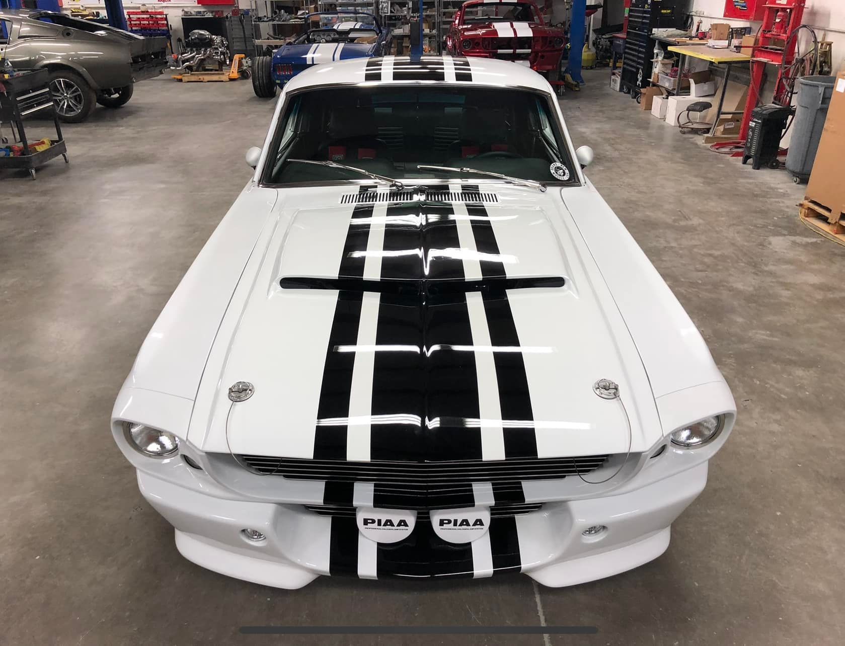 White vintage car with black racing stripes in a garage.