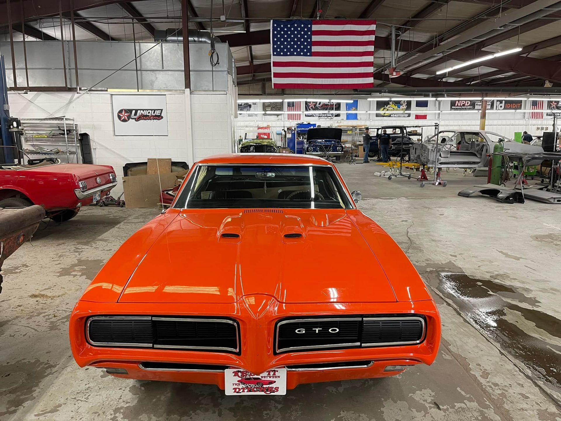 Bright orange vintage Pontiac GTO muscle car in a garage with an American flag.