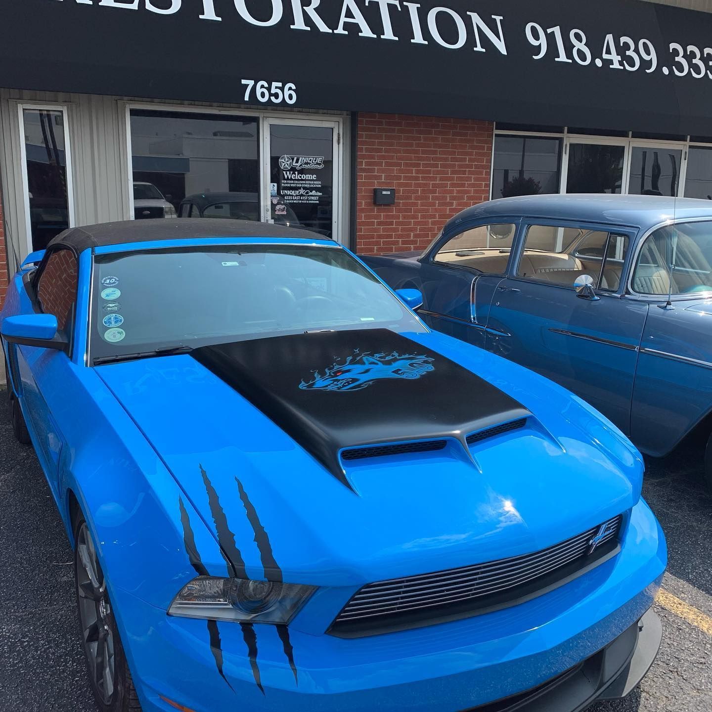 Blue Mustang and classic blue car parked outside a building with 