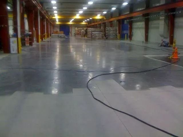 Wide, polished concrete factory floor with overhead lighting and equipment.
