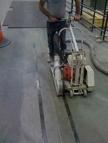 Person using a concrete saw to cut a line in a concrete floor.