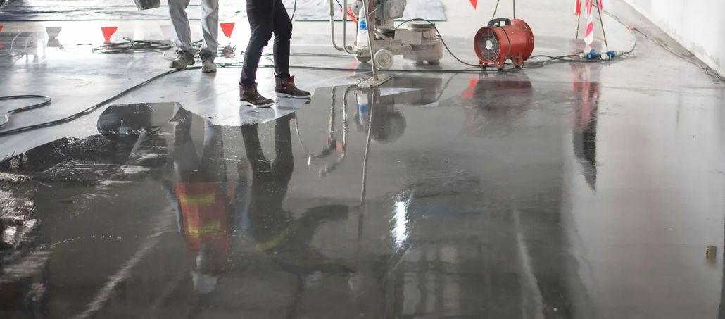 Person working on a wet concrete floor, with construction equipment and reflections.