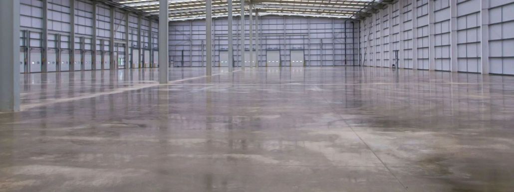 Interior of a large, empty warehouse with reflective concrete floor and metal walls.