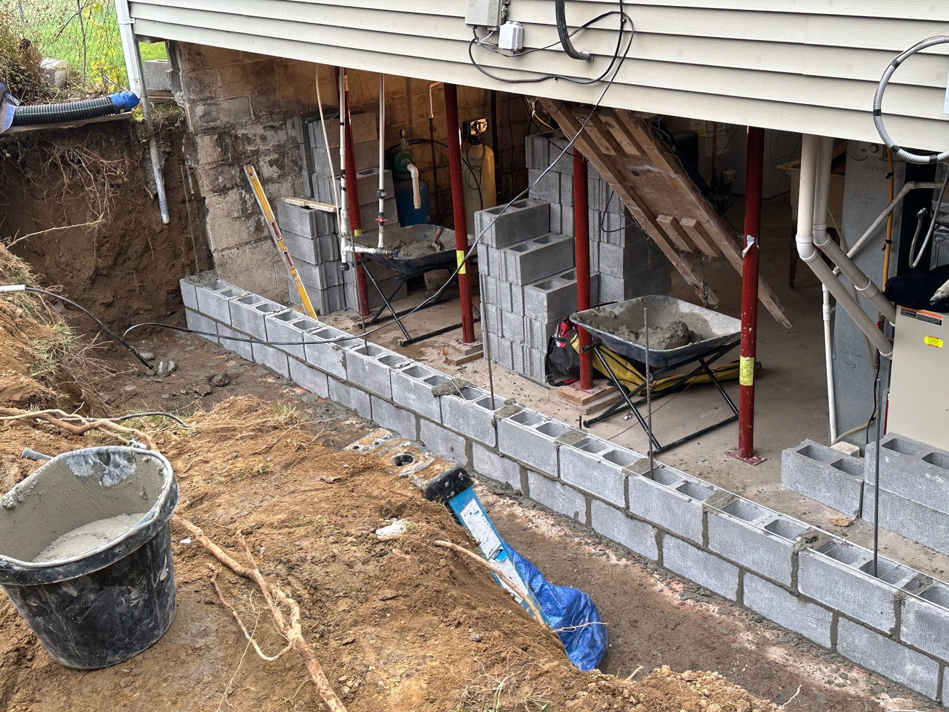 A bucket of cement is sitting in the dirt next to a brick wall being built.