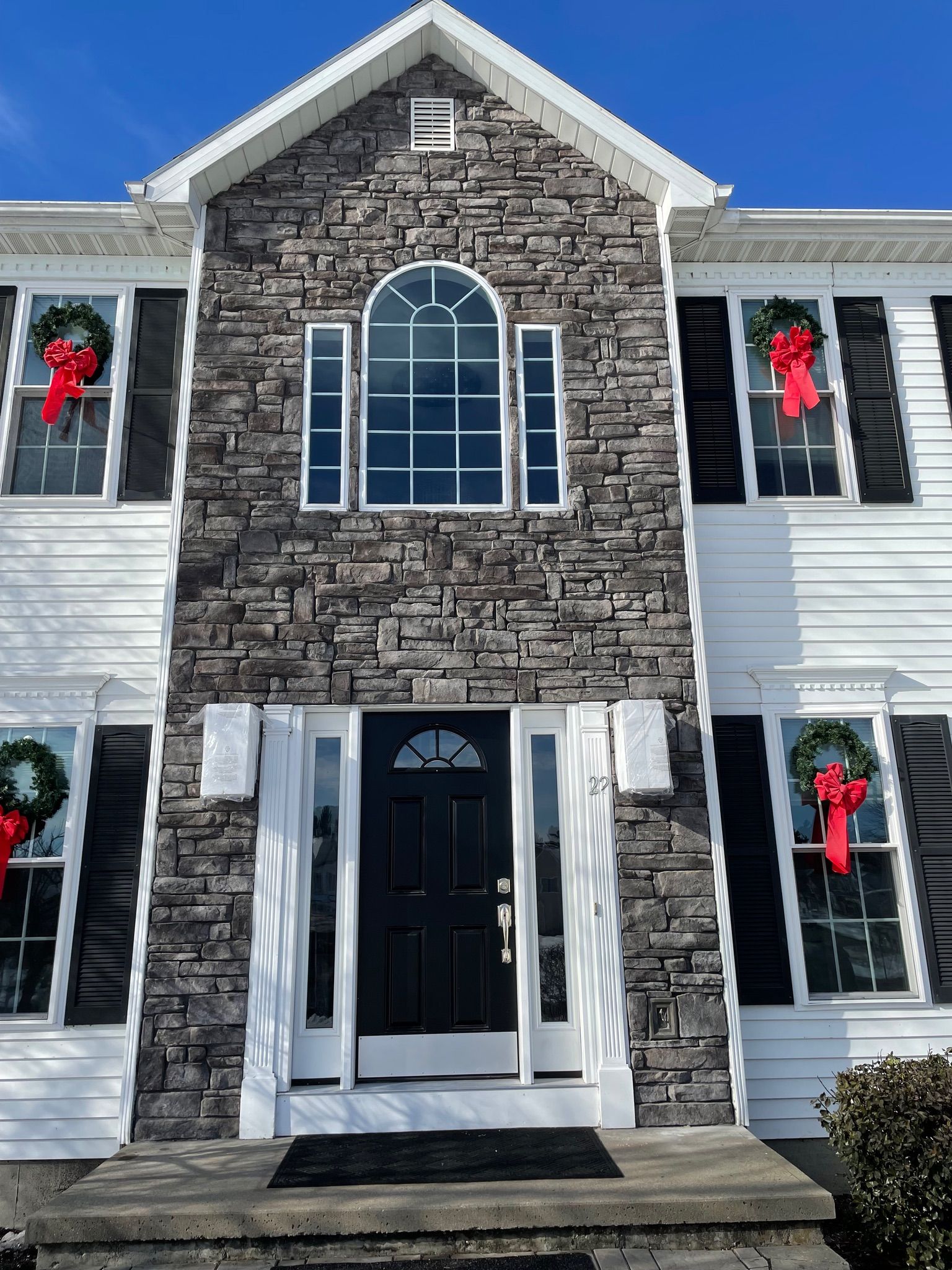 A large stone house with black shutters and a black door is decorated for christmas.