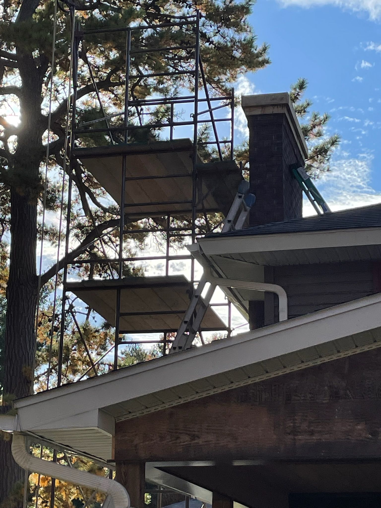 A scaffolding is sitting on top of a house next to a chimney.