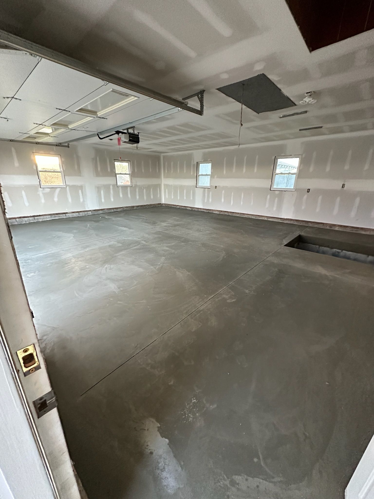An empty garage with a concrete floor and a garage door open.