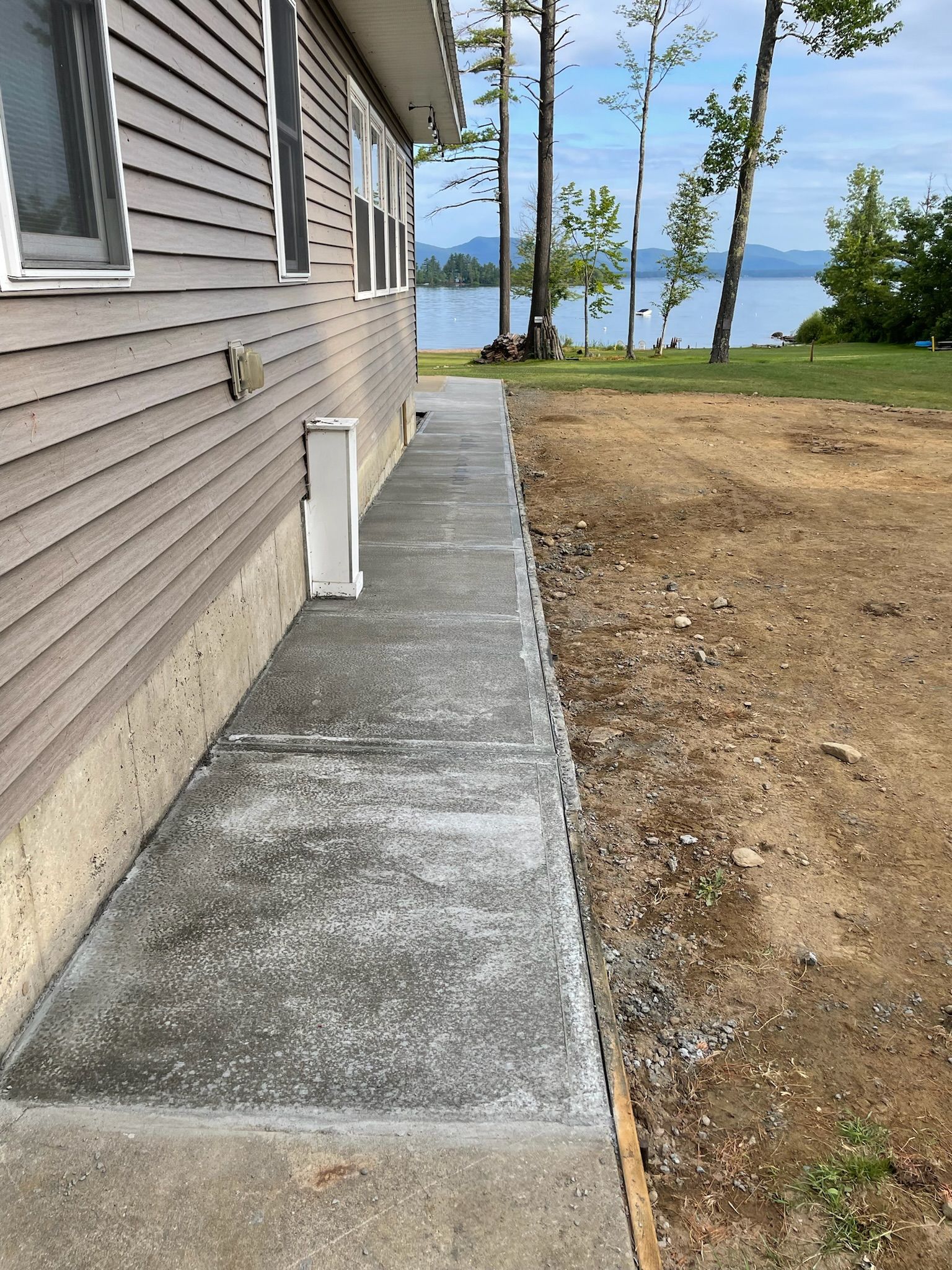 A concrete walkway leading to a house with a view of a lake.