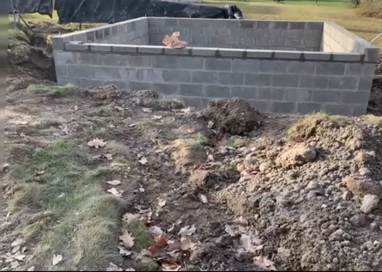 A brick wall is being built in a yard next to a pile of dirt.